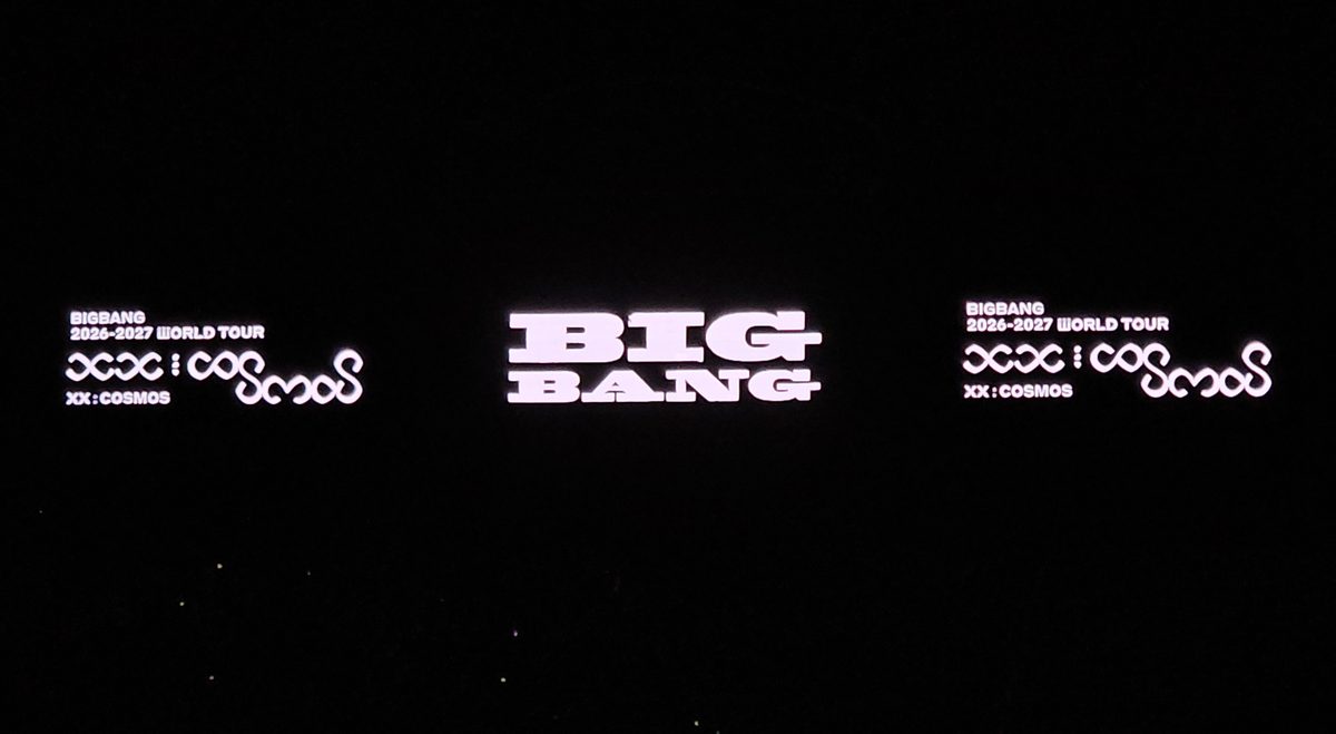 A dark stadium stage with BIG BANG glowing in white block letters on the centre screen, flanked by the XX: COSMOS 2026–2027 world tour logo on two side screens.
